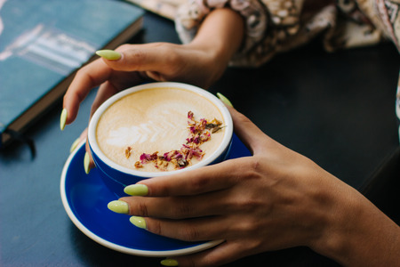 Coffee cup with latte art on wooden background in female hands. Beautiful foam, brown ceramic cup, space for text and design.の写真素材