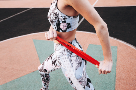 Girl doing hand exercises with a red rubber band at the stadium.の写真素材