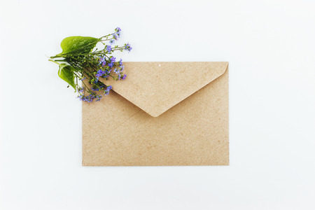Little cute blue forget-me-nots in a Kraft paper envelope, selective focus. Beautiful bouquet of blue flowers bruners on a light background. Flat lay.の写真素材