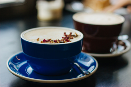 Two cups of cappuccino with latte art on black background. Beautiful foam, blue and brown ceramic cups, stylish toning, place for design and text.の写真素材