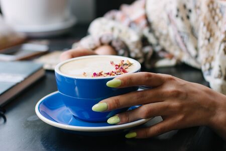 Coffee cup with latte art on wooden background in female hands. Beautiful foam, brown ceramic cup, space for text and design.の写真素材