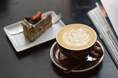A Cup of coffee with latte art with a delicious piece of cake. Beautiful foam, brown ceramic Cup, space for design and text.の写真素材