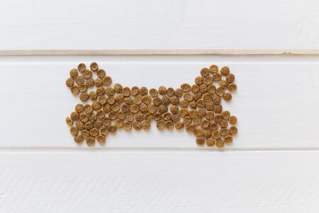 Dry animal feed in the shape of a bone on a white wooden background. Cat eats dry food. Food for...