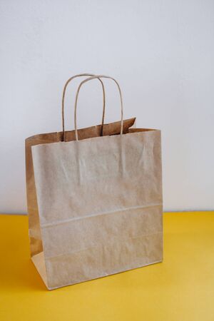 A paper bag and a beautiful succulent on a yellow table. Simple brown paper bag for lunch or meal. The layout for the design. Environmental ship packages.の写真素材