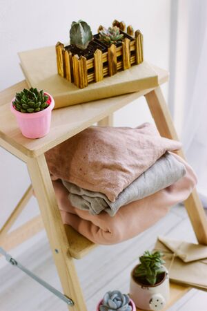 Several warm sweaters on a wooden shelf on a light background. Autumn and winter clothes. Small plants in pretty pots. Succulents, envelopes with letters. A stack of three warm sweaters.の写真素材