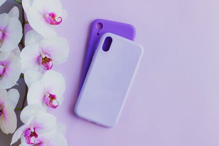 A branch of a beautiful Orchid and two silicone cases for your smartphone. Silicone mobile phone cases of lilac and purple colors lie on a pastel background. Selective focus.の写真素材