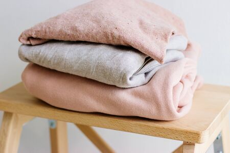 Several warm sweaters on a wooden shelf on a light background. Autumn and winter clothes. A stack of...