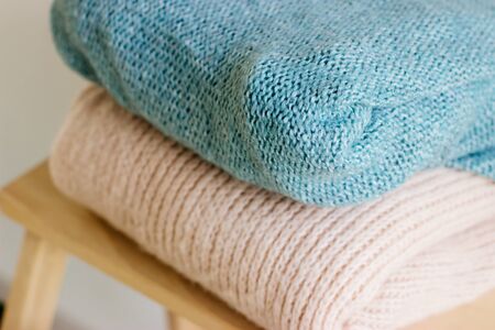 Several warm sweaters on a wooden shelf on a light background. Autumn and winter clothes. A stack of...