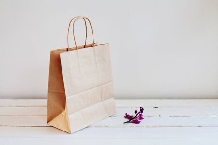 A sprig of purple Orchid and a bag of brown environmental paper on a light background. A paper bag...