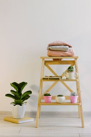 Several warm sweaters on a wooden shelf on a light background. Autumn and winter clothes. Small plants in pretty pots. Succulents, envelopes with letters. A stack of three warm sweaters.の写真素材