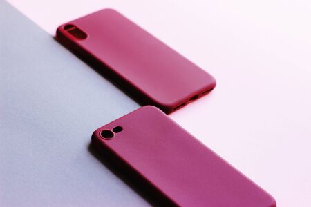 Two cases on the smartphone are on a gray-pink background. Silicone covers of red and delicate pink colors. Covers with holes for the camera.の写真素材