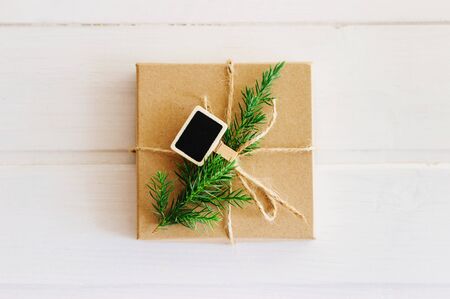 Gift box with fir branch and clothespin for decoration on white wooden background, copy space. Christmas composition with a gift box made of Kraft paper. Selective image focus.の写真素材