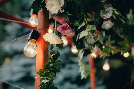 Decoration wedding arch with white and pink flowers on a green natural background. Decorative garland of light bulbs. Wedding decor, light bulbs on a wooden frame. Selective focus.の写真素材