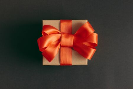 Composition with gift box made of Kraft paper. The box is decorated with a bow of red satin ribbon. Selective image focus.の写真素材