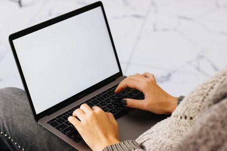 The girl works at the computer. A laptop with a white screen on her lap. The girl works at the computer in a cafe. Marble tiles in the background.の写真素材