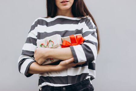 A girl in a striped jumper embraces two gifts. Beautiful girl on a gray background with gift boxes in her hands. Girl holding gifts. Gift for Christmas, birthday, Valentine's Day.の写真素材