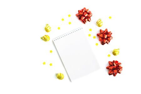 A notebook on an isolated white background. Golden Christmas balls, stars, three red shiny bows. Selective focus.の写真素材