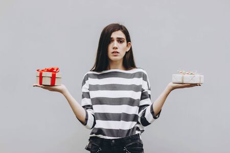 A girl in a striped jumper with two gifts in her hands. A girl with long hair in a black and white jumper holds a gift tied with a red satin ribbon. Difficult choice of gift. Selective focus.の写真素材
