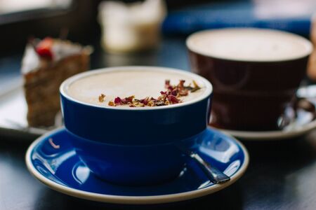 Two cups of cappuccino with latte art on black background. Beautiful foam, blue and brown ceramic cups, stylish toning, place for design and text.の写真素材