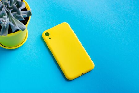 Yellow silicone cover for the smartphone. A smatphone case and a pot of succulent on a blue background. Selective focus.の写真素材