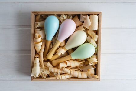 Colorful maracas in a wooden box with shavings. Wooden rattles for toddlers. Children's safe toys.