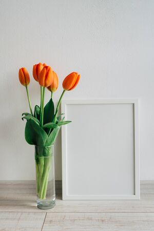 Poster frame mockup. White wooden frame for painting, photo or poster. Bright orange bouquet of...