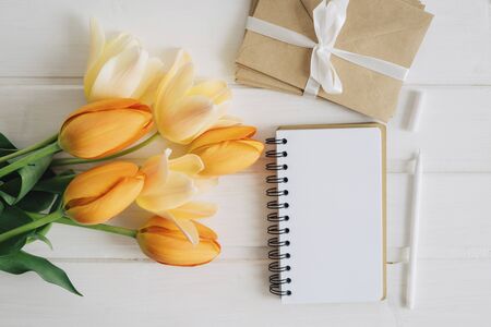 A notebook with a clean white sheet, a bouquet of beautiful flowers, craft ingess bandaged with white satin ribbon, a handle lie on a white wooden table. Flat lay.の写真素材
