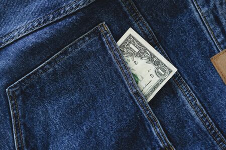One dollar bill sticks out of the back pocket of jeans. Money, currency.