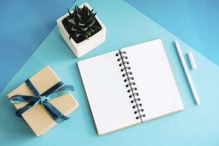 An open notebook, succulent in a white pot and a gift box. Gift craft box tied with a velvet...