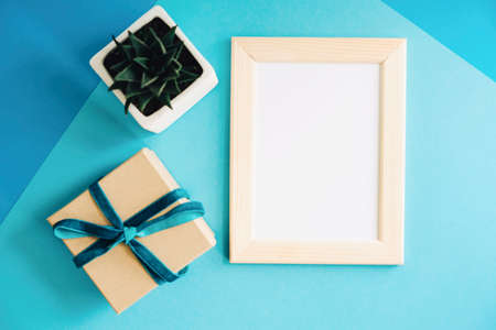 Gift box, wooden frame with a white sheet of paper and a pot with a room flower. A template for design or text.の写真素材