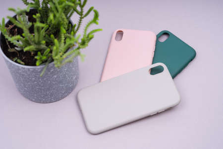 A few silicone cases for the smartphone. Grey, green and pink smartphone cases. Protect your phone. Green plant in a gray pot.の写真素材