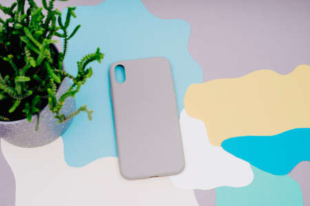 Protective covers for the smartphone. The gray silicone case for the smartphone lies on an abstract background. background of gray, yellow, white, green and blue. Pot with a house plant.の写真素材
