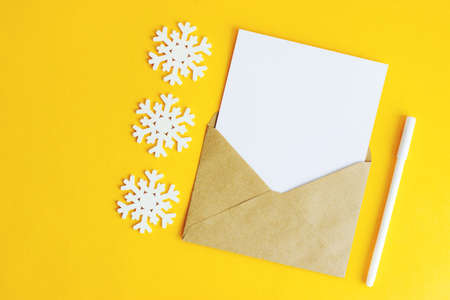 An envelope with a white letter sheet and wooden snowflakes on a yellow background. Christmas...