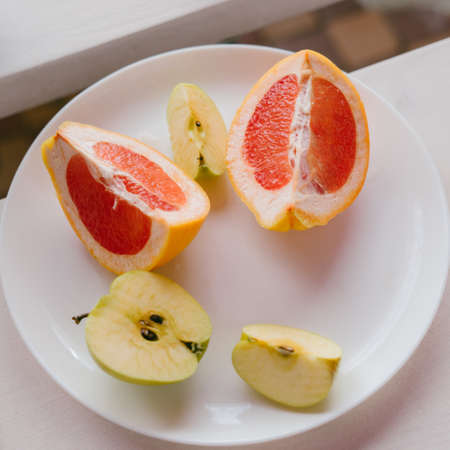 A plate of fruit. Grapefruit and apples are cut on a white plate.