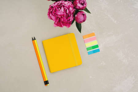 Back to school. A bouquet of pink peonies, a yellow notebook, colored sticky bookmarks and simple...