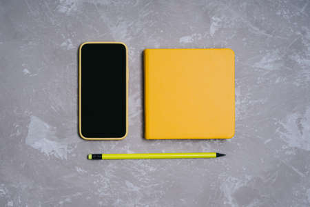 Back to school. A set of yellow items on a gray background. Smartphone in a yellow silicone case, a simple pencil and notepad or sketchbook.の写真素材