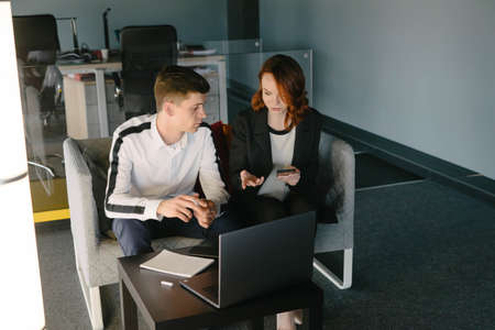 Two young people discuss a business project. A guy and a girl are sitting at their laptops and...