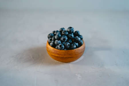 A small wooden bowl with berries on a gray background. Juicy and ripe blueberries in an eco-friendly dish. The concept of healthy eating and nutrition.の写真素材