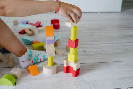 Childrens hands build a house from wooden cubes.
