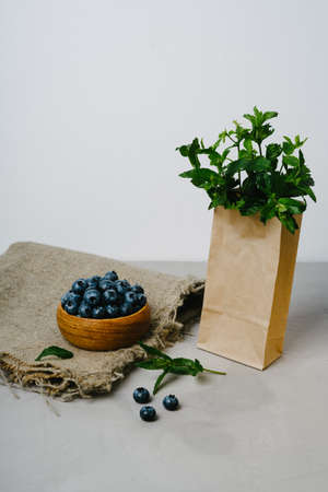 Eco package with fresh mint and wooden bowl with blueberries. Delicious and juicy berries in dishes made of natural material.の写真素材
