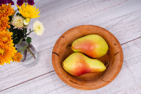 Happy Thanksgiving. A wooden plate with a scented pear. A bouquet of autumn flowers and a ripe juicy pear. The dishes are made of natural material. Delicious fruits in wooden utensils.の写真素材