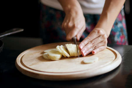 Girl cuts a young potato on a wooden board. The process of cooking.の写真素材