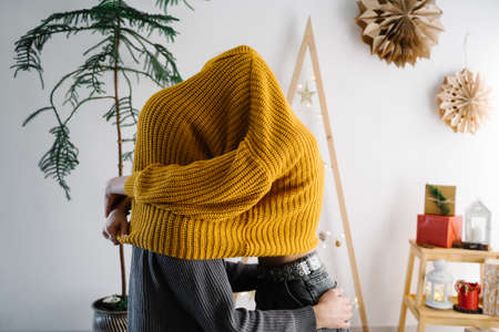 Girl and her boyfriend kiss hiding under her yellow sweater. Christmas decor in the background. Live...