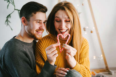 Couple of lovers look at a heart of two canes. Christmas romance. Christmas decor. Yellow and gray popular colors of 2021. Hand made ecological wooden Christmas tree.の写真素材