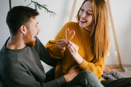Couple of lovers look at a heart of two canes. Christmas romance. Christmas decor. Yellow and gray popular colors of 2021. Hand made ecological wooden Christmas tree.の写真素材