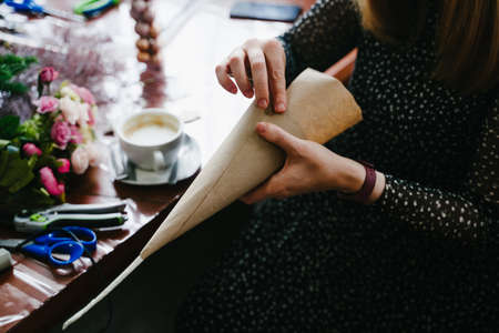 A girl wraps a foam cone in kraft paper for a Christmas craft. Nobilis branches in the background. Close-up of hands. New Year's Eve master class on creating decorations from natural nobilis.の写真素材
