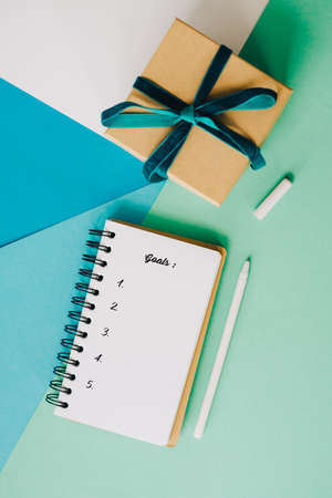 Notebook to write down goals for 2022. A houseplant, a notebook and a pen lie on an abstract...