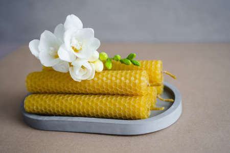 Candles made of honey wax on a gray oval tray. White freesia flowers.