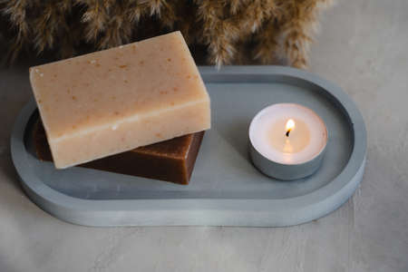 Handmade soap and a plate on a gray background. Eco-friendly products. Oval plaster gray tray with natural soap. The candle is burning.の写真素材