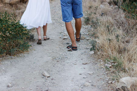 Close up of legs. A girl and a guy are walking along a dirt mountain trail. People's feet are...